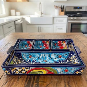 May include: A set of hand-painted ceramic serving dishes. The set includes a large rectangular tray with handles, and three smaller square dishes. The dishes feature a vibrant floral design in blue, red, and yellow on a dark blue background.