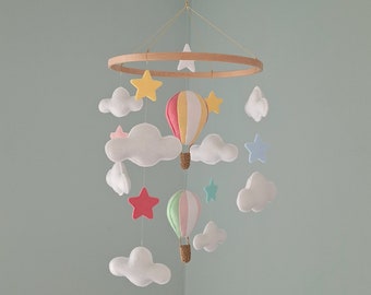 May include: A wooden ring mobile with felt clouds, stars, and hot air balloons. The balloons are pink, yellow, and green with white stripes. The clouds are white and the stars are yellow, pink, blue, and red.