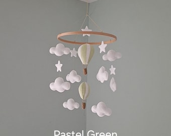 Könnte beinhalten: Ein Mobile mit einem pastellgrünen Heißluftballon, weißen Wolken und Sternen. Das Mobile ist aus Filz und an einem Holzring aufgehängt.