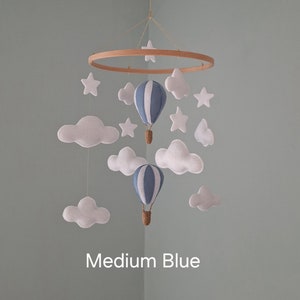 May include: A baby mobile with a wooden ring, white clouds, blue and white striped hot air balloons, and white stars. The mobile is labelled "Medium Blue".