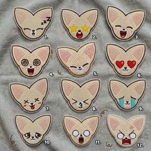 May include: A collection of twelve embroidered patches featuring a stylized fox design with various facial expressions. The patches are beige with pink inner ears and a white outline, showcasing emotions like sleep, surprise, and anger.