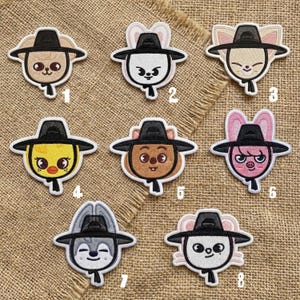 May include: Set of eight embroidered patches featuring cartoon animal faces wearing black hats. Each patch has a unique animal design, including a bear, rabbit, fox, duck, and pig. The patches are outlined in white and set against a tan fabric background.