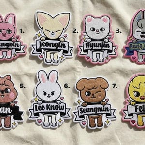 Pode incluir: Uma coleção de oito patches bordados com personagens de animais de desenho animado. Cada patch tem um design único, incluindo um coelho, uma raposa, um urso, um cão e um pintinho. Cada personagem segura uma faixa com um nome, como "Changbin" ou "Felix".
