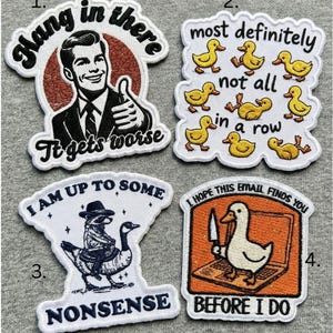 Op de afbeelding: Vier geborduurde patches met humoristische ontwerpen. Eén toont een man die een duim omhoog steekt met de tekst "Hang in there, it gets worse". Een andere toont eendjes met de tekst "most definitely not all in a row". Een derde toont een wasbeer die op een gans rijdt met de tekst "I am up to some nonsense". De laatste toont een eend met een mes en de tekst "I hope this email finds you before I do."