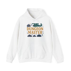 Puede incluir: Sudadera con capucha blanca con bolsillo delantero y el texto "DUNGEON MASTER" en dorado y azul. El diseño incluye dados y un gráfico de dragón, ideal para los fanáticos de los juegos de rol.