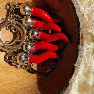 Könnte beinhalten: Eine Sammlung roter Chilihorn-Schlüsselanhänger mit silberfarbenen Metallakzenten und Schlüsselringen. Die Schlüsselanhänger sind in einer Holzschale angeordnet und zeigen ihre leuchtende Farbe und ihr Design.