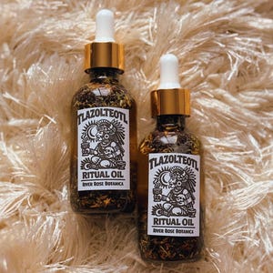 May include: Two glass bottles of ritual oil with gold-colored caps and white droppers. Each bottle has a label with the text "Tlazolteotl Ritual Oil River Rose Botanica" and a black and white illustration of a figure.