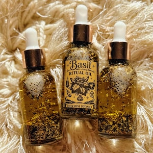 May include: Three glass bottles of Basil Ritual Oil with gold-colored liquid and herbs. Each bottle has a white dropper and a copper-colored cap. The label reads "Basil Ritual Oil" and "River Rose Botanica" with botanical illustrations.
