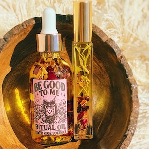 Puede incluir: Un frasco cuentagotas de vidrio transparente y un frasco roll-on alto y delgado llenos de aceite dorado y trozos botánicos secos. El frasco cuentagotas tiene una etiqueta rosa con el texto BE GOOD TO ME RITUAL OIL RIVER ROSE BOTANICA.