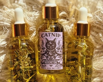 May include: Three glass bottles of catnip ritual oil with gold-colored caps and droppers. The bottles have a light amber hue and contain herbs. One bottle has a label with a black cat illustration and the word "CATNIP".