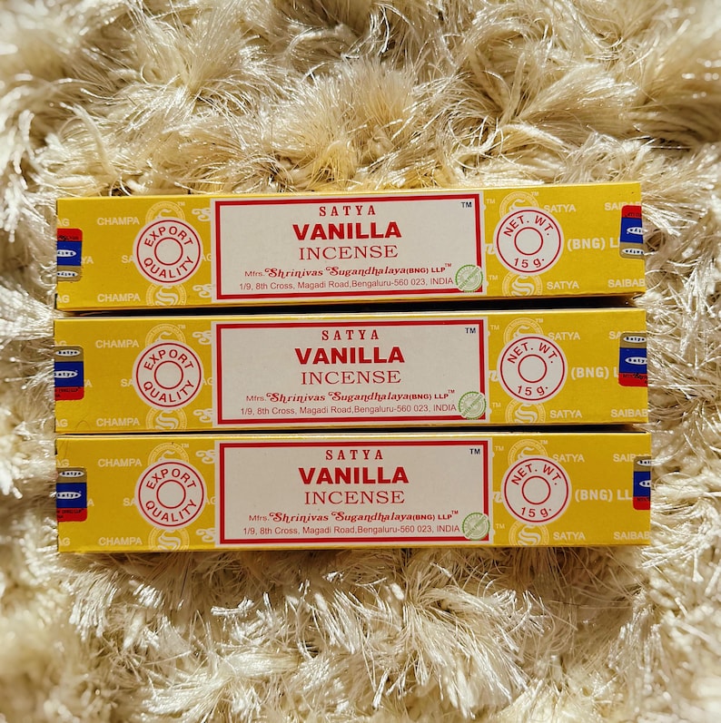 May include: Three boxes of Satya Vanilla Incense are stacked on a textured surface. Each box is yellow with red and white text, including "Vanilla Incense" and "Export Quality." The net weight is 15g.