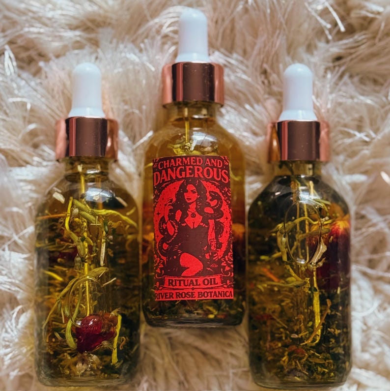 Pu&ograve; includere: Tre bottiglie di vetro di olio rituale con contagocce bianchi e collari color rame. La bottiglia centrale ha un'etichetta rossa con una donna e le parole "Charmed and Dangerous". Le bottiglie sono piene di erbe e fiori.