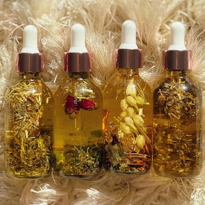 May include: Four clear glass dropper bottles filled with golden liquid and botanical ingredients. Each bottle has a white dropper top with a rose gold collar. The bottles contain herbs, flowers, and other natural elements, creating a visually appealing and aromatic product.