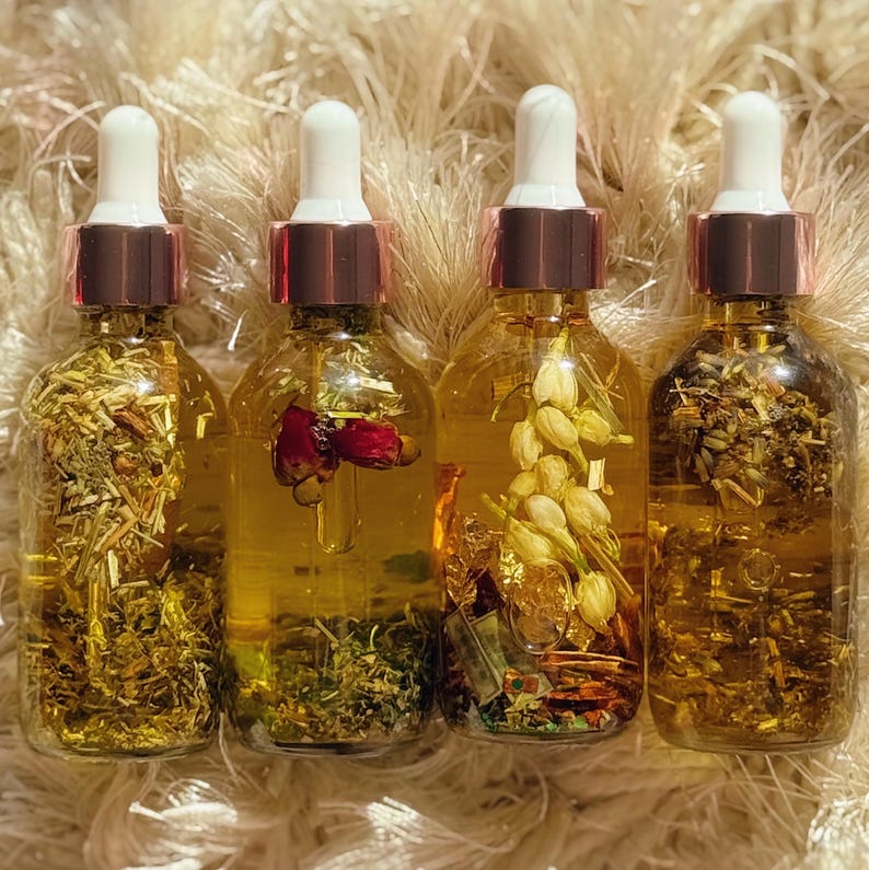 May include: Four clear glass dropper bottles filled with golden liquid and botanical ingredients. Each bottle has a white dropper top with a rose gold collar. The bottles contain herbs, flowers, and other natural elements, creating a visually appealing and aromatic product.