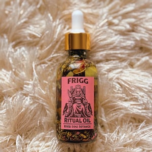 Könnte beinhalten: Eine klare Glasflasche mit Frigg Ritual Oil und einem goldenen Tropfaufsatz. Das rosa Etikett zeigt eine Illustration einer sitzenden Frau und den Text "RITUAL OIL" und "River Rose Botanica". Die Flasche enthält sichtbare Kräuter.