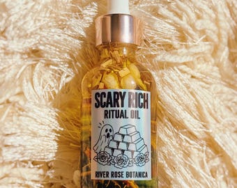 Può includere: Un flacone contagocce in vetro trasparente riempito con olio dorato e frammenti botanici. L'etichetta riporta la scritta SCARY RICH RITUAL OIL, RIVER ROSE BOTANICA e presenta un disegno a inchiostro nero di un fantasma, lingotti d'oro e rose.
