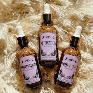 以下が含まれることがあります： ドロッパー付きの「Motivation Ritual Oil」のガラス瓶3本。各ボトルには、目、三日月、ろうそく、「Motivation Ritual Oil」と「River Rose Botanica」の文字が入った紫色のラベルが付いています。ボトルには金色の液体とハーブが入っています。
