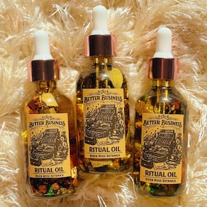 May include: Three glass ritual oil bottles with white droppers and copper-colored collars. Each bottle has a label that reads "Better Business Ritual Oil" with a vintage cash register illustration. The bottles are filled with herbs.