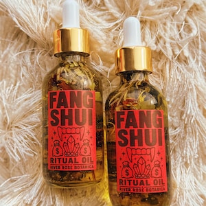Könnte beinhalten: Zwei klare Glastropfflaschen gefüllt mit botanischem Öl und getrockneten Kräutern. Jede Flasche hat einen goldfarbenen Verschluss und ein rotes rechteckiges Etikett mit schwarzem Text FANG SHUI RITUAL OIL RIVER ROSE BOTANICA und einer Grafik von Fangzähnen.