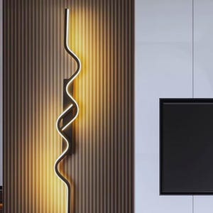 Può includere: Una moderna applique da parete nera con un design ondulato e illuminato di bianco. L'apparecchio è montato su una parete marrone a strisce verticali. Lo sfondo comprende una parete bianca e un elemento rettangolare nero.
