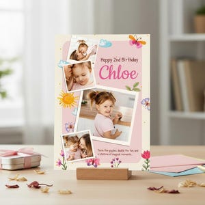 May include: A personalized birthday card for a 2-year-old named Chloe, featuring multiple photos, butterflies, and floral accents. The card is displayed on a wooden stand, with a gift box and stationery nearby.