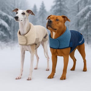 Puede incluir: Dos perros con abrigos de invierno de pie en la nieve. Uno es blanco con un abrigo beige, el otro es marrón con un abrigo azul marino. El abrigo beige tiene la palabra "Zuri". El abrigo azul marino tiene la palabra "Peanut".