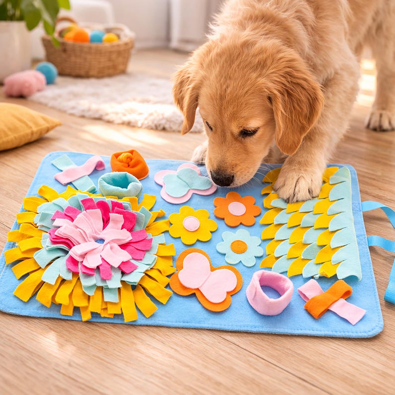 Op de afbeelding: Een blauwe vilten hondenactiviteitenmat met kleurrijke vilten vormen, waaronder bloemen, een vlinder en linten. De mat is ontworpen om de zintuigen van een hond te stimuleren en mentale verrijking te bieden. Een golden retriever puppy interacteert met de mat.