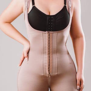 Peut inclure: Un vêtement gainant beige intégral avec des bretelles réglables et une fermeture éclair sur le devant. Le vêtement comprend un soutien-gorge intégré et s'étend jusqu'à mi-cuisse avec une bordure en dentelle. Le shapewear est conçu pour lisser et galber le corps.
