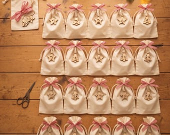 May include: An advent calendar set consisting of twenty-four small off-white fabric drawstring bags, each tied with a red and white checkered ribbon and featuring a wooden tag numbered one through twenty-four in various shapes like stars and trees.