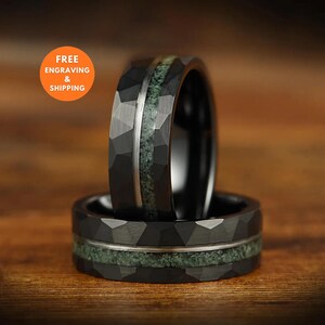 Puede incluir: Un anillo negro con una superficie exterior geom&eacute;trica facetada y una incrustaci&oacute;n central de material texturizado en color verde salvia. La banda presenta una fina franja de metal plateado pulido que recorre horizontalmente el centro.