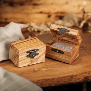 Puede incluir: Dos cajas rectangulares de madera con vetas distintivas y cierres de metal color bronce de estilo antiguo. Una caja est&aacute; cerrada, mientras que la otra est&aacute; abierta, revelando un forro de tela gris texturizada en el interior de la base.