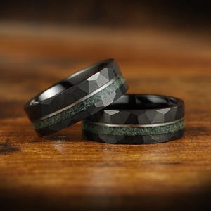 Puede incluir: Dos anillos negros con un acabado exterior facetado y martillado. Cada banda presenta una incrustaci&oacute;n horizontal central de material triturado texturizado en color verde salvia, separada de los bordes oscuros por una fina l&iacute;nea plateada.