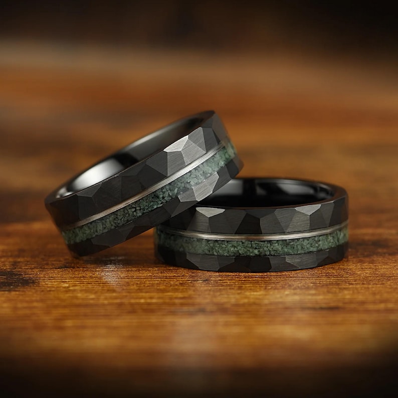 Puede incluir: Dos anillos negros con un acabado exterior facetado y martillado. Cada banda presenta una incrustaci&oacute;n horizontal central de material triturado texturizado en color verde salvia, separada de los bordes oscuros por una fina l&iacute;nea plateada.