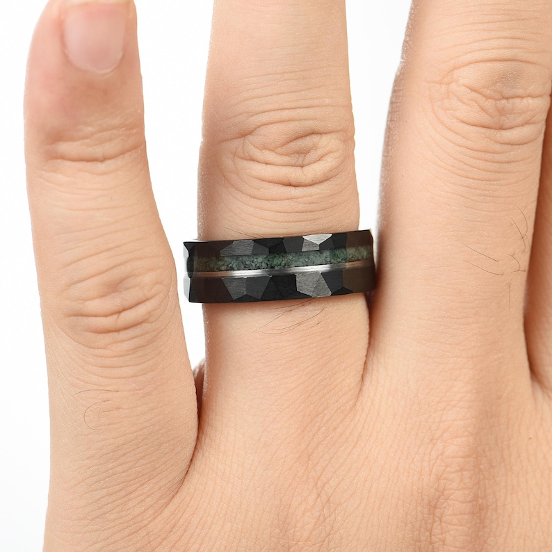 Puede incluir: Un anillo negro con una textura de superficie geom&eacute;trica facetada. La banda presenta una incrustaci&oacute;n horizontal de material texturizado de color verde musgo en el centro, separada de los bordes negros por una fina l&iacute;nea met&aacute;lica plateada.