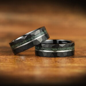 Puede incluir: Dos anillos negros con una superficie exterior facetada. Cada anillo presenta una incrustaci&oacute;n horizontal central de material verde texturizado, separada del metal negro por una fina banda plateada lisa que recorre la circunferencia.