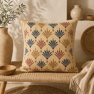 Peut inclure: Coussin carré beige avec un motif répété en forme d'éventail bleu marine, rouge et or. Le coussin est placé sur un banc tressé, avec des vases décoratifs et un bol en arrière-plan. Le coussin ajoute une touche d'élégance à n'importe quelle pièce.