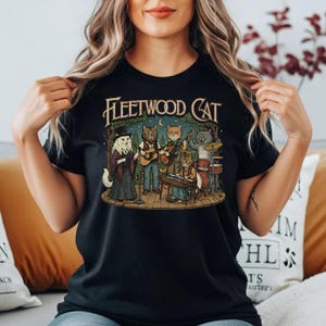 May include: Black t-shirt with the text "Fleetwood Cat" and an illustration of a cat band. The band includes a cat singer, guitarists, a keyboardist, and a drummer. The design has a vintage, concert poster style.