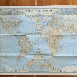 May include: A vintage paper world map titled A MAP OF THE WORLD, published by The National Geographic Magazine. The map features two large circular hemispheres with light blue oceans and tan landmasses, including four smaller corner globes.