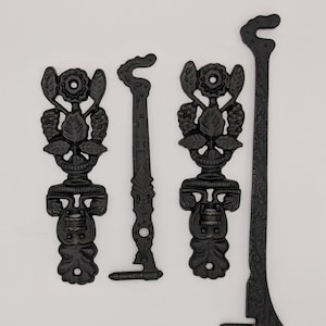 May include: Four black metal decorative pieces. Two pieces have a floral design at the top and a decorative base. Two other pieces are long and curved, with a hook shape at the top and a decorative design.