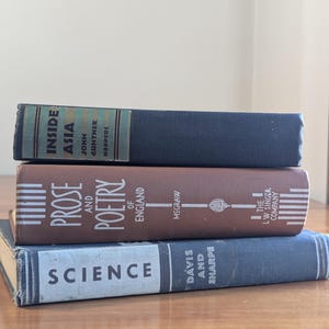 May include: A stack of three vintage books with titles visible: "Inside Asia," "Prose and Poetry of England," and "Science." The books are in shades of blue, brown, and gray, with text and decorative elements on their spines.