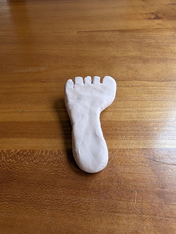 A genuine vintage 1970s hand-sculpted white clay foot brooch — anatomically odd, folk-art charming, and a hilariously perfect gift for a podiatrist or body-horror jewelry fan.
