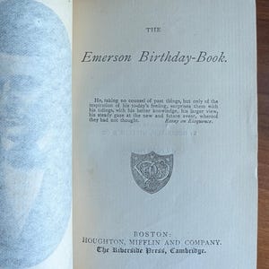 Puede incluir: P&aacute;gina abierta de un libro con el t&iacute;tulo "Emerson Birthday-Book". El texto incluye una cita de un ensayo sobre la elocuencia. El libro es publicado por Houghton, Mifflin and Company en Boston.