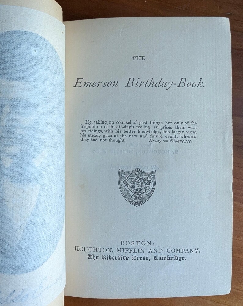 Puede incluir: P&aacute;gina abierta de un libro con el t&iacute;tulo "Emerson Birthday-Book". El texto incluye una cita de un ensayo sobre la elocuencia. El libro es publicado por Houghton, Mifflin and Company en Boston.