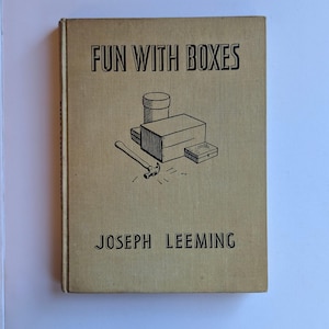 May include: A tan hardcover book titled Fun With Boxes by Joseph Leeming. The front cover features a black line drawing of a hammer, a cylindrical container, and two rectangular boxes. The text is printed in a bold, black, sans-serif font.