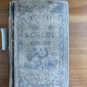 May include: An antique book titled "Reed's Gradual Course on School Arithmetic" with a worn, light-colored cover. The cover features faded blue text and decorative elements, with the publisher's name and location, Boston, visible.