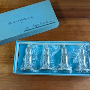 May include: A set of four silver-colored salt and pepper shakers in a blue box. The box is labeled "Glass Lined Salt & Pepper Shakers" and "Empire Silver Co."