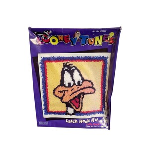 May include: A Looney Tunes Latch Hook Kit featuring Daffy Duck. The kit is packaged in a purple bag with the Looney Tunes logo and the text "Latch Hook Kit". The finished size is approximately 13 x 13 inches.