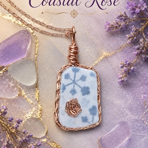 Puede incluir: Un collar con colgante rectangular que presenta un fragmento de cerámica blanca con un patrón floral azul, envuelto en alambre de oro rosa. El colgante cuelga de una cadena de oro rosa a juego. El texto Coastal Rose y Design by Mariel es visible.