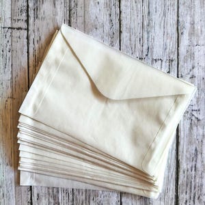 May include: A stack of cream-colored paper envelopes with a triangular flap design. The envelopes are rectangular in shape and feature a smooth, matte finish. The stack consists of multiple individual envelopes layered neatly on top of each other.