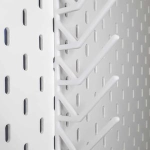 May include: White pegboard with several white hooks attached. The hooks are designed to hold items and are mounted on a white pegboard with evenly spaced holes. The hooks are angled and project outward.